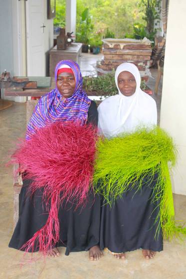 Two artisans holding bundles of bright dyed palm leaf