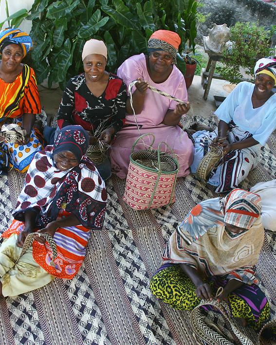 Women of the MOTO cooperative sitting together weaving palm leaf on a finished mat