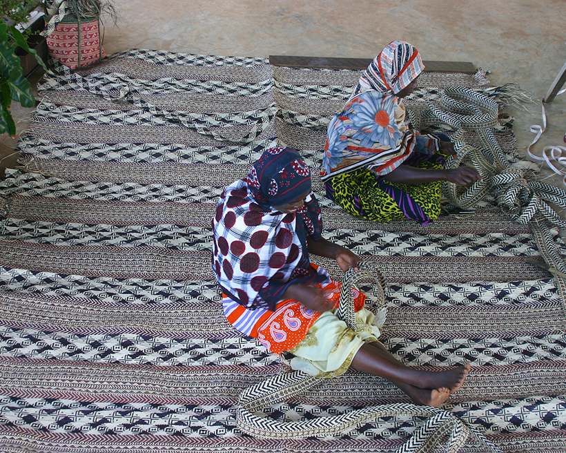 Two women plaiting bright green palm leaf together on the floor of the Pete workshop